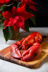 Whole cooked red lobster on a wooden cutting board. Red poinsettia plant in pot. Festive dinner ingredients for Christmas table.
