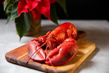 Whole cooked red lobster on a wooden cutting board. Red poinsettia plant in pot. Festive dinner ingredients for Christmas table.