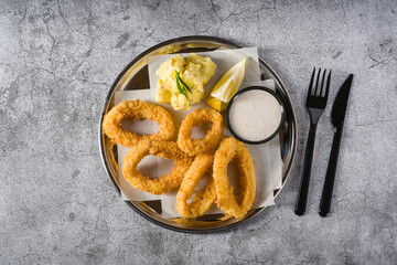 Fried calamari with potato salad next to it on stone table
