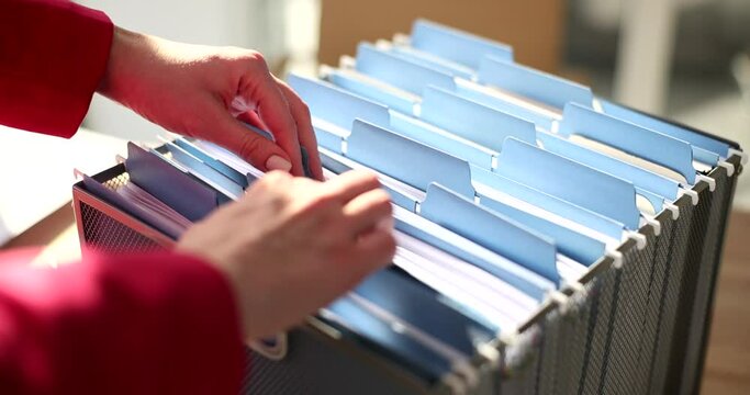 The hands of a business woman sort through documents in a box, close-up. Organization of information on the topic