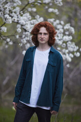 Red-haired young man in a white tee and dark jacket, with spring blossoms in the background