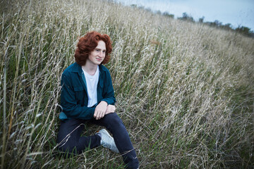 Curly redhead man sitting in a field, casual and pensive