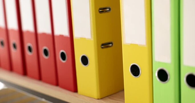 The hand takes out a yellow folder from a series of folders on the rack, a close-up. Choosing a ring binder