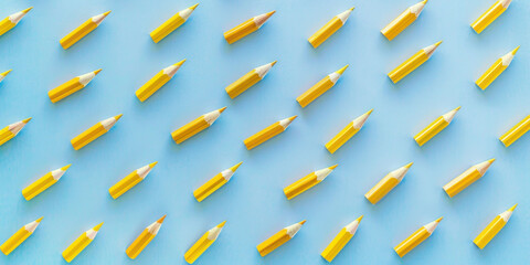 Vibrant arrangement of many yellow pencils on blue background with clear blue sky, creating a colorful and eyecatching pattern