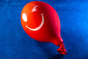 A deflated red balloon. Red winking inflatable balloon with a smile