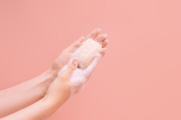 Naklejka premium Female soapy hands holding a piece of soap against a pink background.