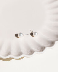 Pair of pearl stud earrings on cream studio background with sunshine