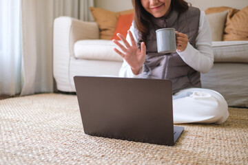 Closeup of a young woman drinking coffee while using laptop computer for video call at home