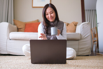 Portrait of a young woman drinking coffee while using laptop computer for video call at home