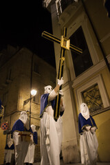 Hooded penitents during the famous Good Friday procession in Chieti (Italy) carry the cross with the effigy of Jesus - 778979957