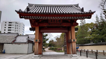 Fukuoka, Japan - 01.28.2020: Front view of Hakata Sennen-no Mon Gate leading to a trail in a garden behind and a truck trimming the garden on the side under a cloudy sky