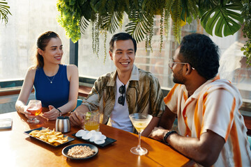Cheerful friends gathered in rooftop pub to have some drinks and talk