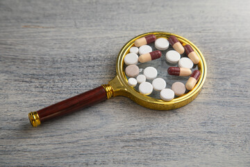 Medical pills with a magnifying glass on the table.