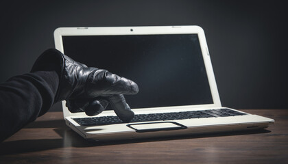 Hacker hand in a leather glove with a computer.