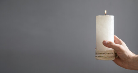Male hand showing white candle on the grey background.