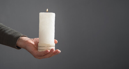 Male hand showing white candle on the grey background.