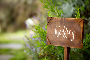 Wooden board with the inscription in paint Wedding. Sign for guests at the entrance, outdoors wedding ceremony decoration. Hand made signboard, welcome wedding wooden plaque with garden on background