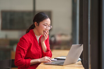 Asian businesswoman in a red shirt is typing on a laptop computer