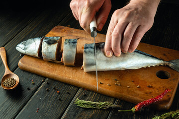 The cook cuts raw mackerel fish on a cutting board before preparing the dish. Low key concept for...