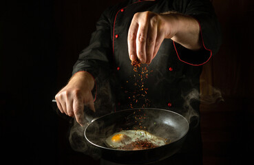 The cook adds aromatic spices to a steaming hot frying pan with fried eggs. Low key concept for a breakfast menu for a hotel with advertising space. Grande cuisine