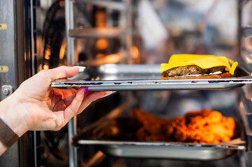 A person pulls a burger tray from an oven, showcasing efficient food prep in a modern kitchen