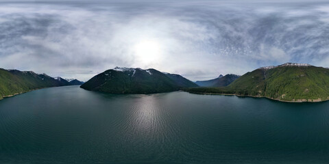 Aerial 360 view of Lake and Mountains. Cloudy Sky.