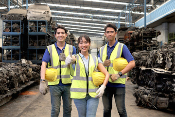 Three of industrial workers wear safety vest, hold helmet, stand together at manufacturing plant...