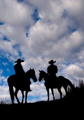 silhouette of two cowboys on horses standing on a hill