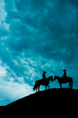 silhouette of two cowboys on horses standing on a hill