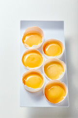 Tray of six eggs with yolks inside. The eggs are arranged in neat row on white stand