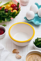 White empty bowl with yellow rim sits on table with other bowls and ingredients.