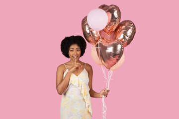 African American woman holding heart-shaped balloons on pink