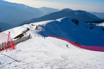 Downhill skiing with skiers in the Caucasus Mountains with silhouettes of mountain peaks far to the...