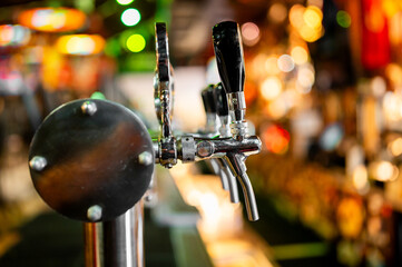 Close-up of beer taps with a blurred background of a bar, highlighting the metallic and black handles, evoking an inviting atmosphere for socializing