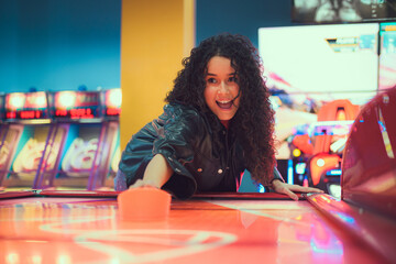 Fototapeta premium Excited young woman enjoying an air hockey game at a vibrant arcade