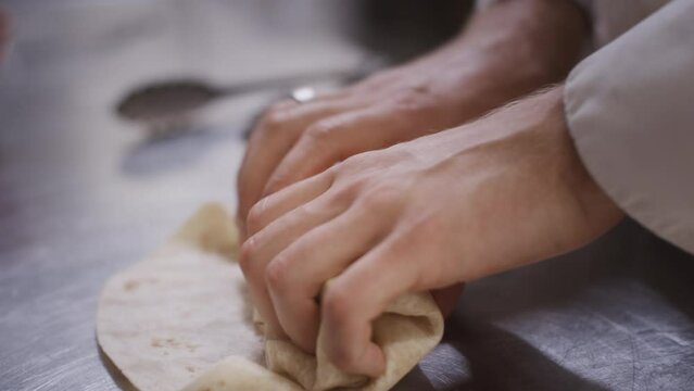 Close-up of a chef finishing the preparation of a wrap in the kitchen.
