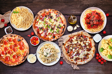 Delicious Italian food table scene. Collection of pizzas and pastas. Overhead view on a dark wood background.