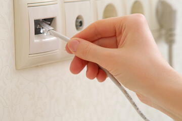 A woman's hand connects the Internet cable to a socket, rj-45