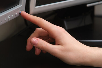 A woman's hand presses the power button on a computer monitor