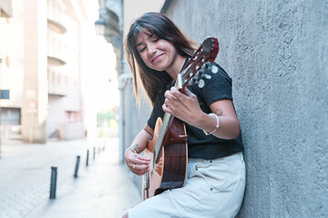portrait of a young musician playing the guitar in the street leaning against a wall