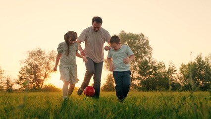 Family team, sports games. Children son daughter play football with father on lawn. Boy girl parent run after red ball in park. Active happy family, child dad having fun playing ball on green grass. - Powered by Adobe