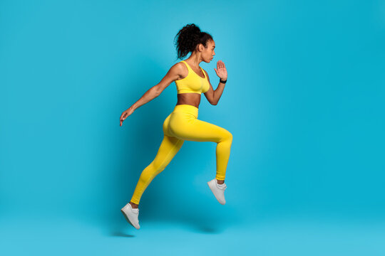 Dynamic female athlete running mid-air on blue background