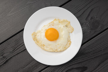 A white plate with a fried egg on a dark wooden surface