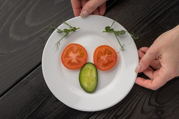 Hand placing pea shoots on a plate with tomato and cucumber slices