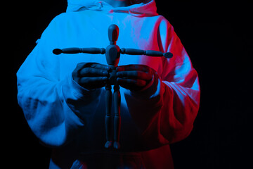 Figure in a hoodie holding a mannequin with arms extended, blue and red hues