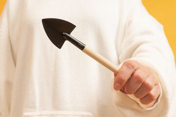 A hand holding a small black garden shovel with a wooden handle