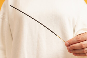 A hand holding a thin black wand with a wooden handle