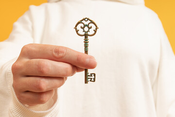 A hand holding an ornate key against a yellow background
