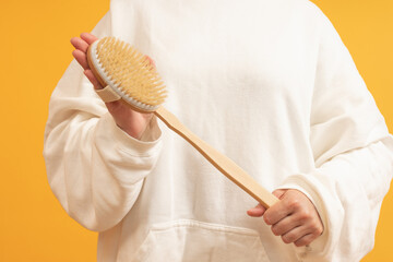 Hand holding a wooden bath brush with a handle