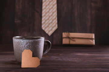 Father's day concept cardboard heart near the mug on the background of a gift and tie on the table